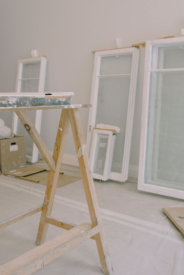 Pièce en cours de remise en état : fenêtres appuyées au mur, tréteau et sol protégé par une bâche